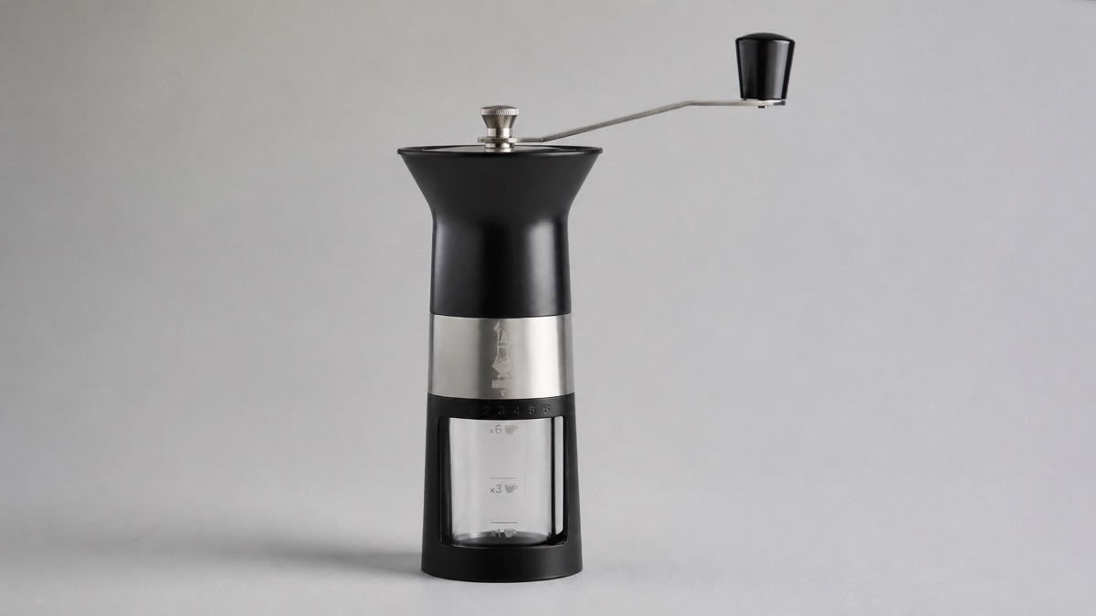 Bialetti manual coffee grinder with a black body, steel band, crank handle and clear marked chamber