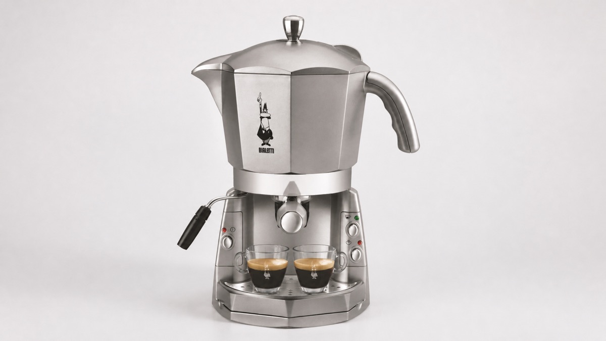 Silver Bialetti Mokona espresso machine with two espresso cups on a plain neutral background