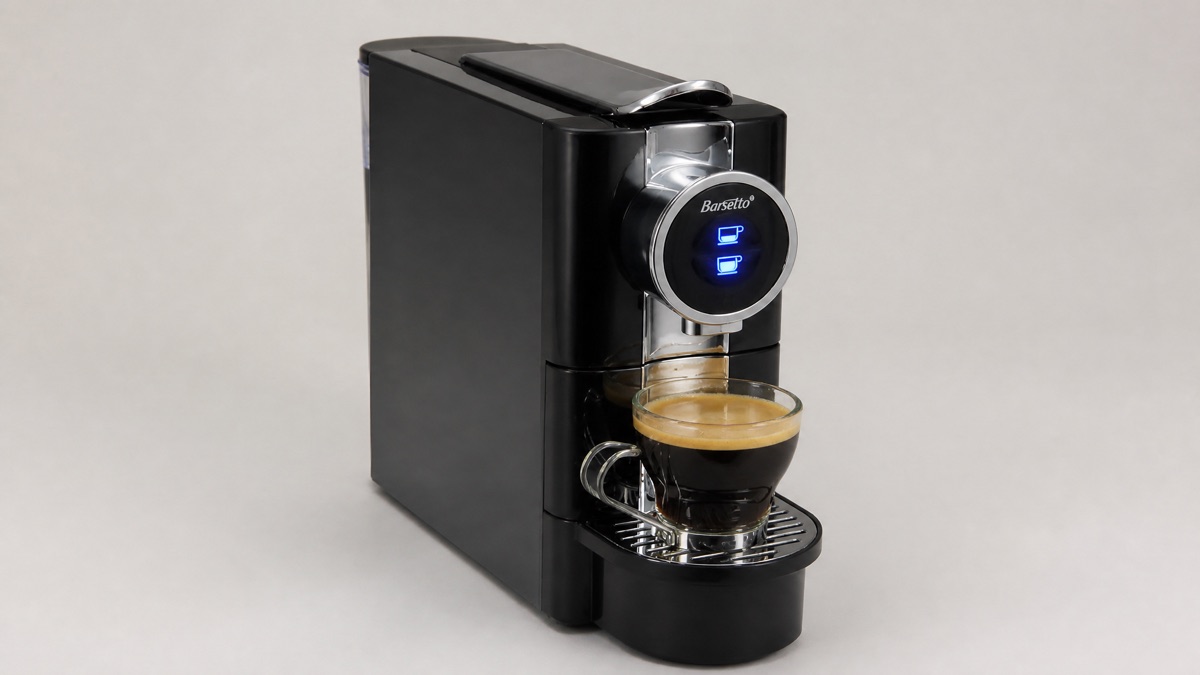 Black Barsetto One-Touch capsule espresso machine with a glass cup of espresso on a plain neutral background