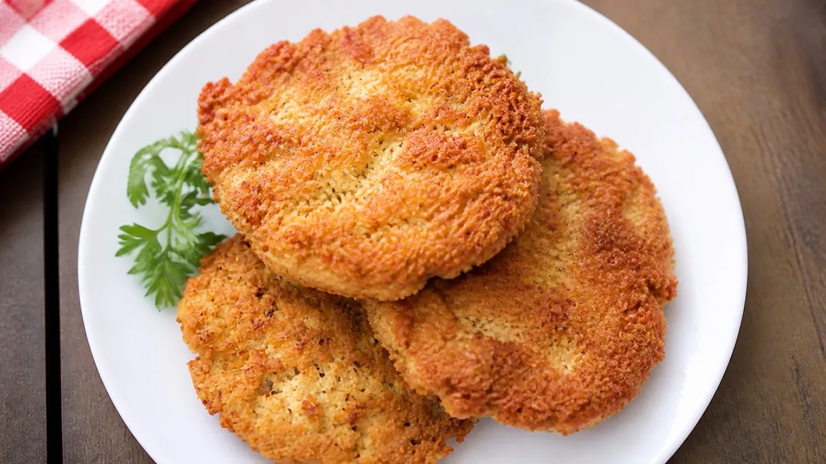 Golden-brown crispy chicken breast patties stacked on a white plate